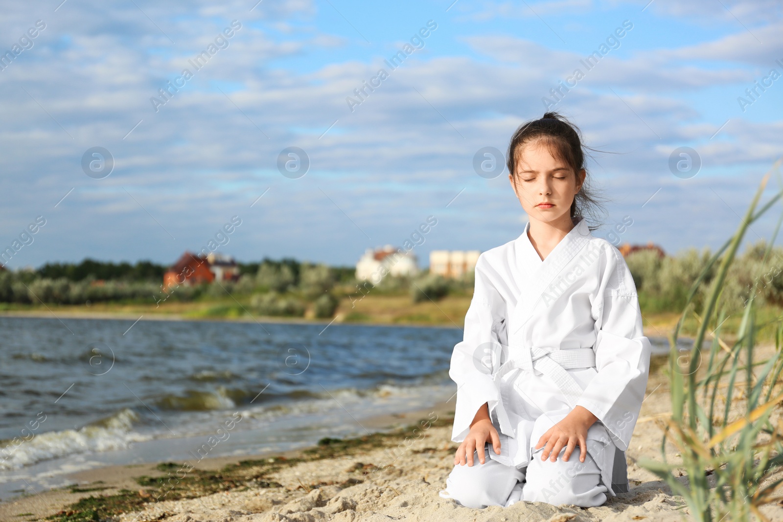 Photo of Cute little girl in kimono meditating near river. Karate practicing