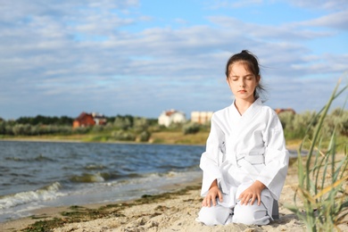 Cute little girl in kimono meditating near river. Karate practicing
