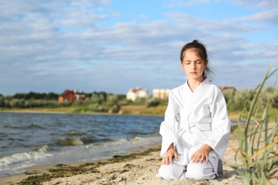 Photo of Cute little girl in kimono meditating near river. Karate practicing