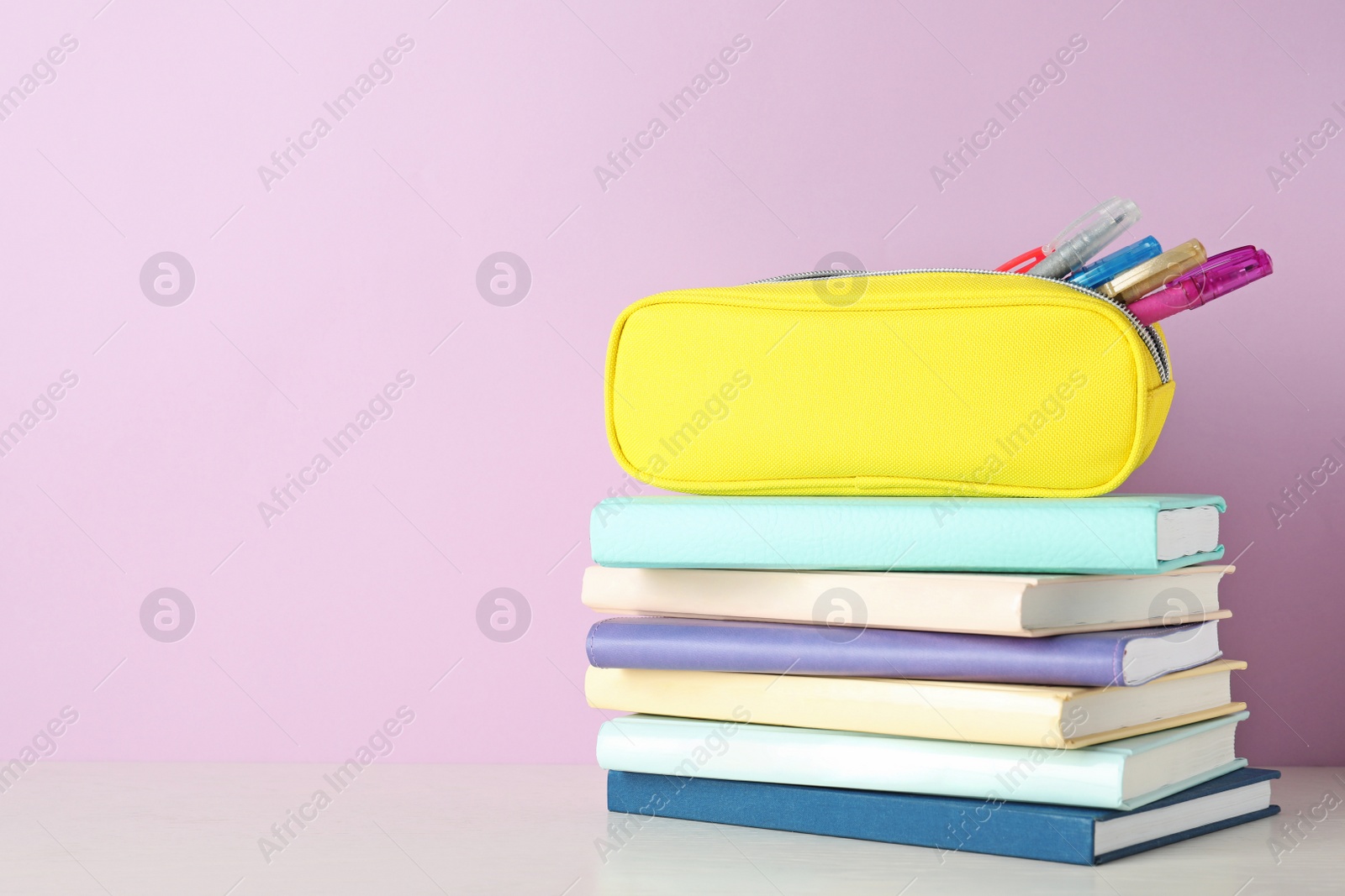 Photo of Stack of books and pen case on table against color background. Space for text