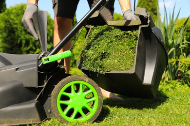 Photo of Man removing grass out of lawn mower box in garden, closeup