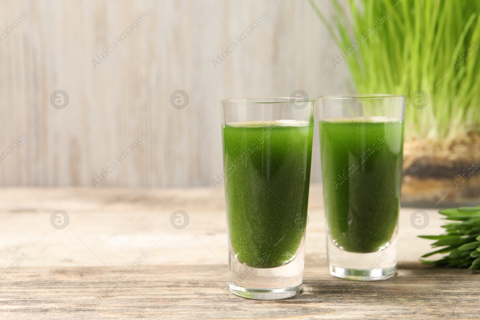 Photo of Wheat grass drink in shot glasses on wooden table, closeup. Space for text