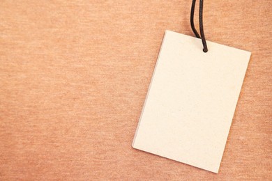 Cardboard tag on brown garment, top view. Space for text