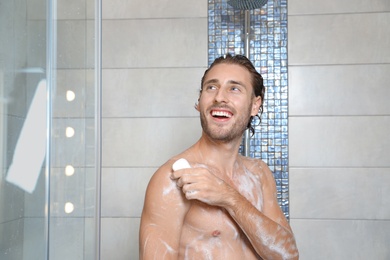 Attractive young man taking shower with soap in bathroom