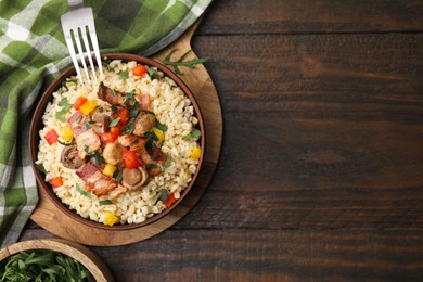 Cooked bulgur with vegetables, fried bacon and mushrooms in bowl on wooden table, top view. Space for text