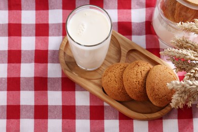 Photo of Glass of milk with cookies on red checkered tablecloth, above view. Space for text