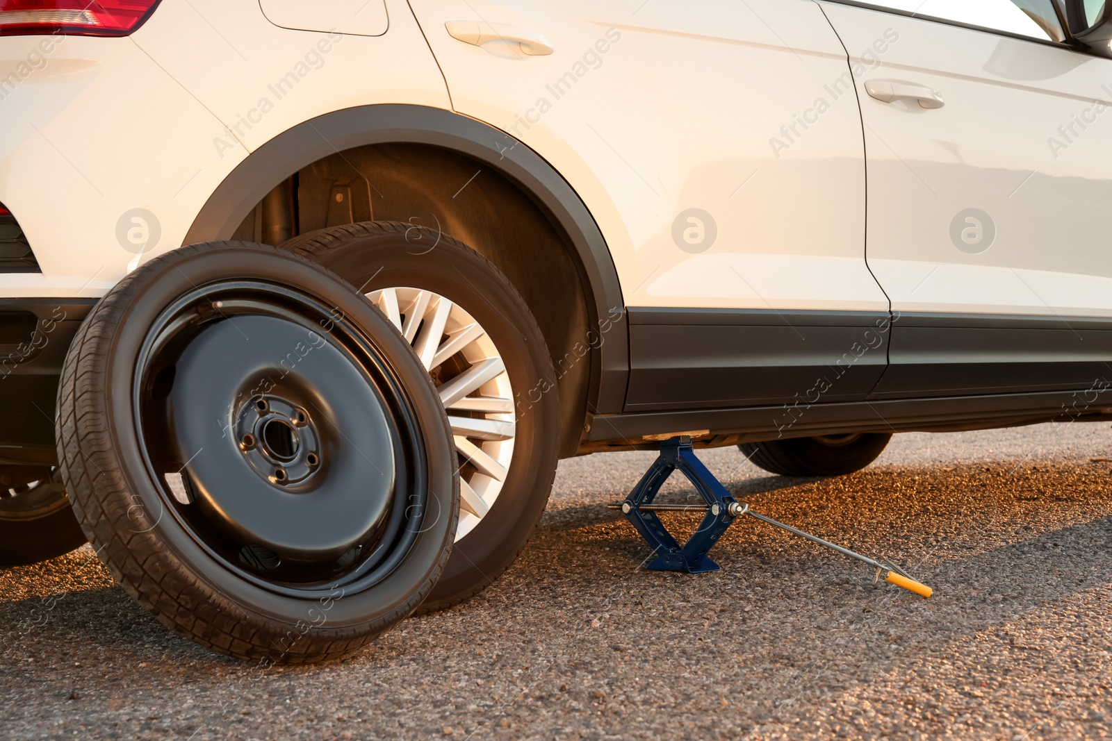 Photo of Car lifted by scissor jack and spare wheel on roadside