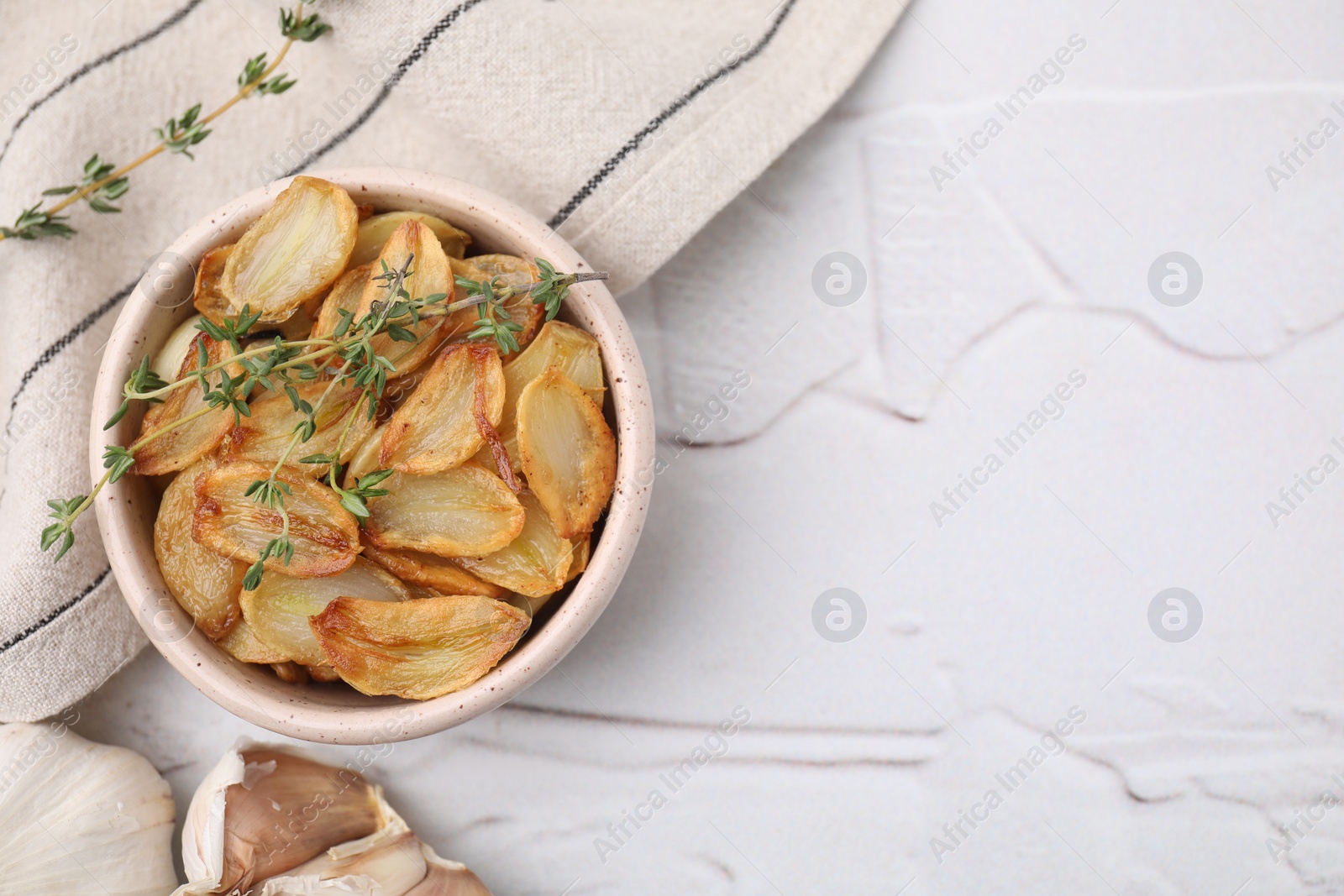 Photo of Fried garlic cloves with thyme in bowl on white table, top view. Space for text