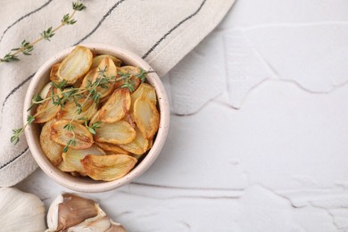 Fried garlic cloves with thyme in bowl on white table, top view. Space for text