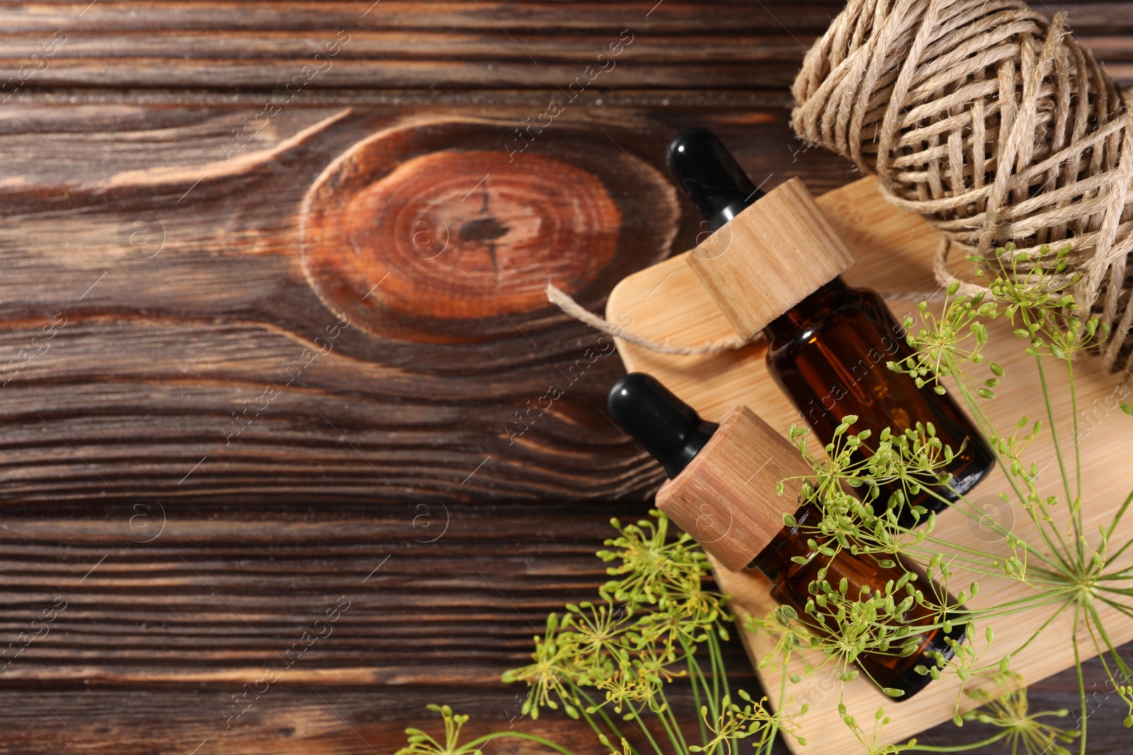 Photo of Bottle of essential oil, fresh dill and twine on wooden table, flat lay. Space for text