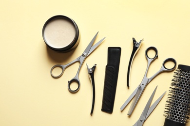 Photo of Scissors and other hairdresser's accessories on light yellow background, flat lay