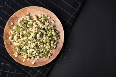 Photo of Wooden plate with sprouted green mung beans on black background, flat lay. Space for text
