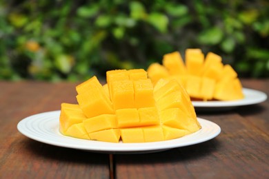 Photo of Delicious ripe cut mangos on wooden table outdoors