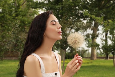 Photo of Beautiful young woman blowing large dandelion in park. Allergy free concept