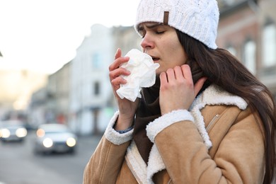Photo of Woman with tissue blowing runny nose outdoors. Cold symptom