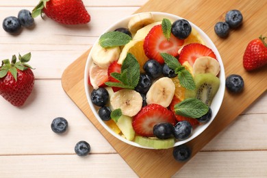Photo of Tasty fruit salad in bowl and ingredients on wooden table, flat lay