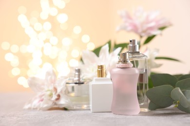 Photo of Bouquet of beautiful lily flowers and perfume bottles on table against beige background with blurred lights, closeup. Space for text