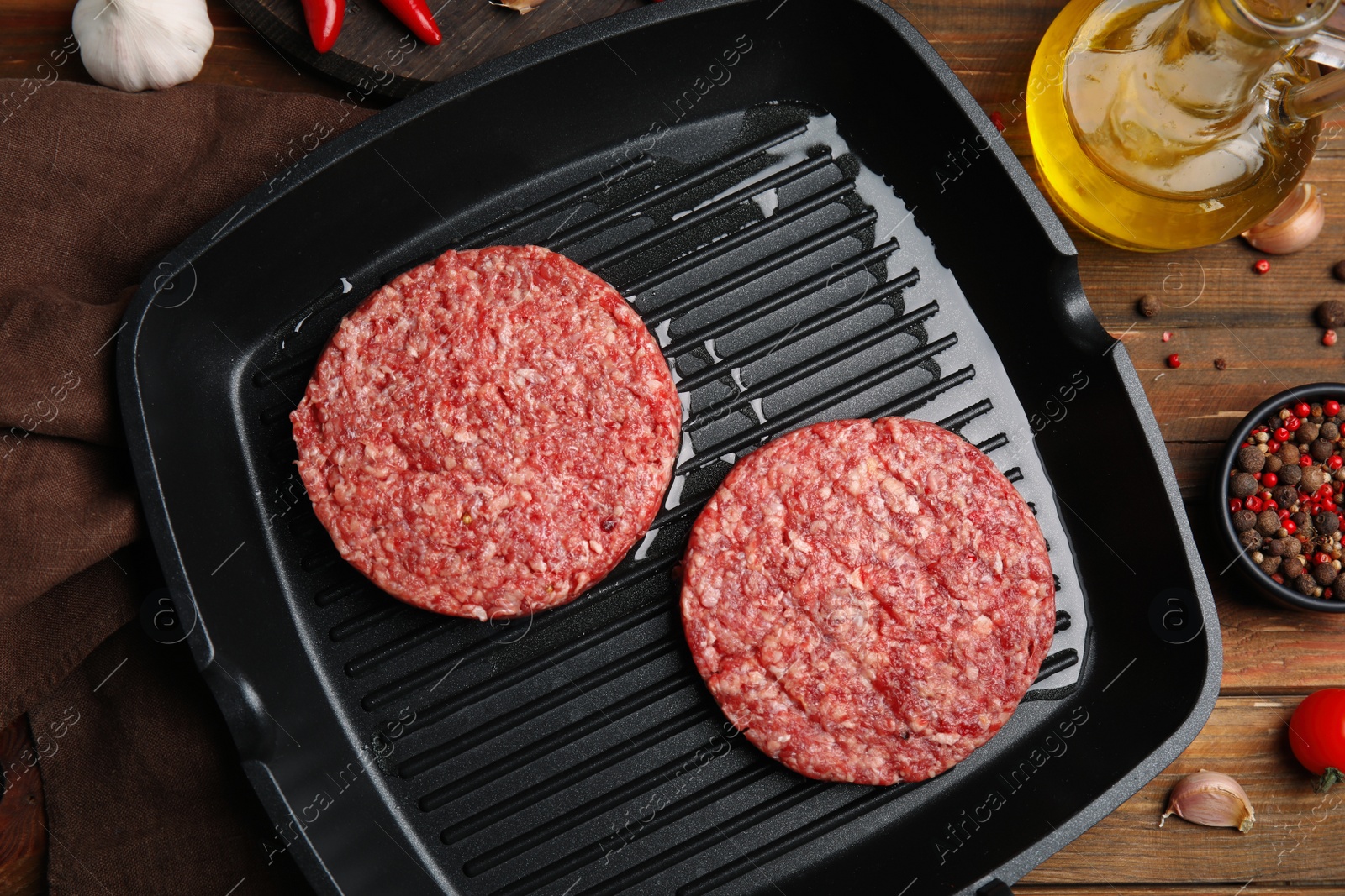 Photo of Raw hamburger patties with oil, vegetables and pepper on wooden table, flat lay