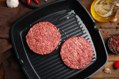 Photo of Raw hamburger patties with oil, vegetables and pepper on wooden table, flat lay