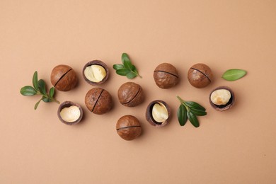 Tasty Macadamia nuts and green leaves on beige background, flat lay