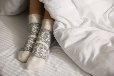 Photo of Woman wearing knitted socks under blanket in bed, closeup