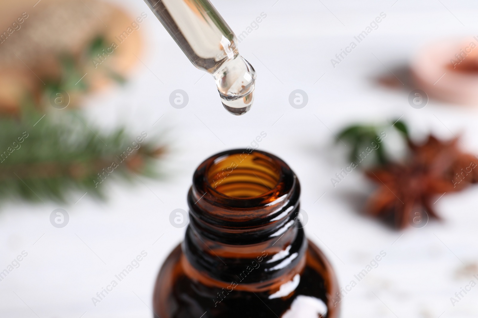 Photo of Dropping anise essential oil from pipette into bottle on table, closeup