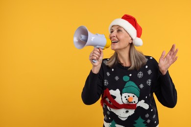 Photo of Senior woman in Christmas sweater and Santa hat shouting in megaphone on orange background. Space for text