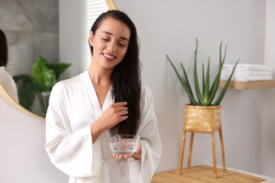 Photo of Young woman holding bowl of aloe hair mask in bathroom. Space for text