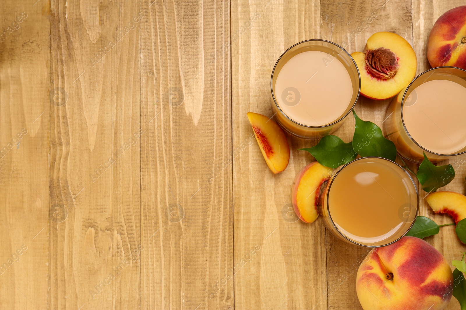 Photo of Glasses of peach juice, fresh fruits and leaves on wooden table, flat lay. Space for text