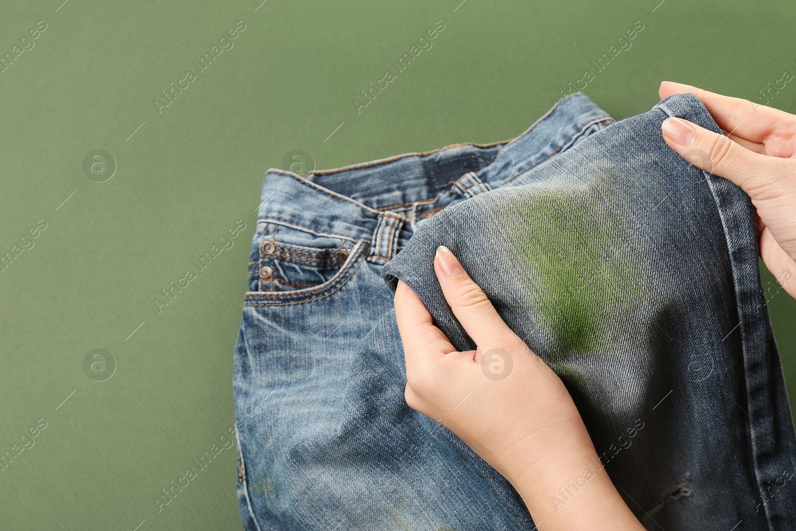 Photo of Woman holding jeans with stain on green background, closeup. Space for text