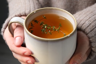 Woman holding cup of tasty herbal tea with thyme, closeup