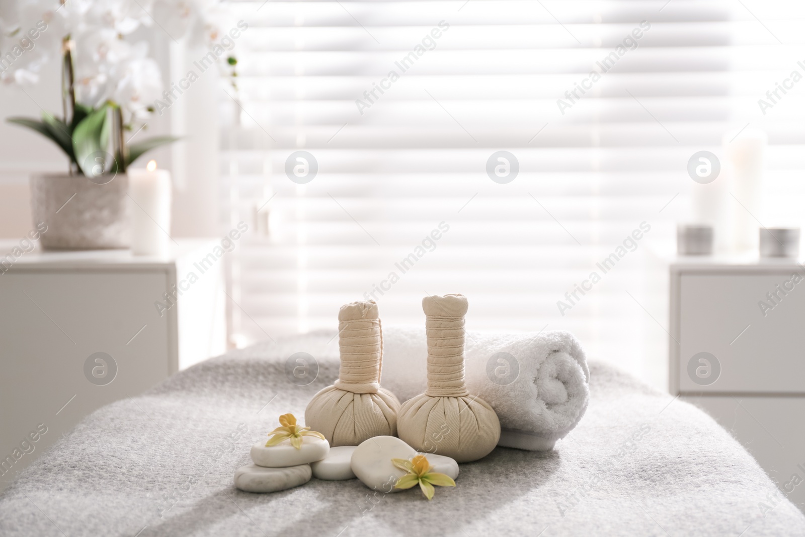 Photo of Herbal bags, orchid flowers and stones on couch in spa salon