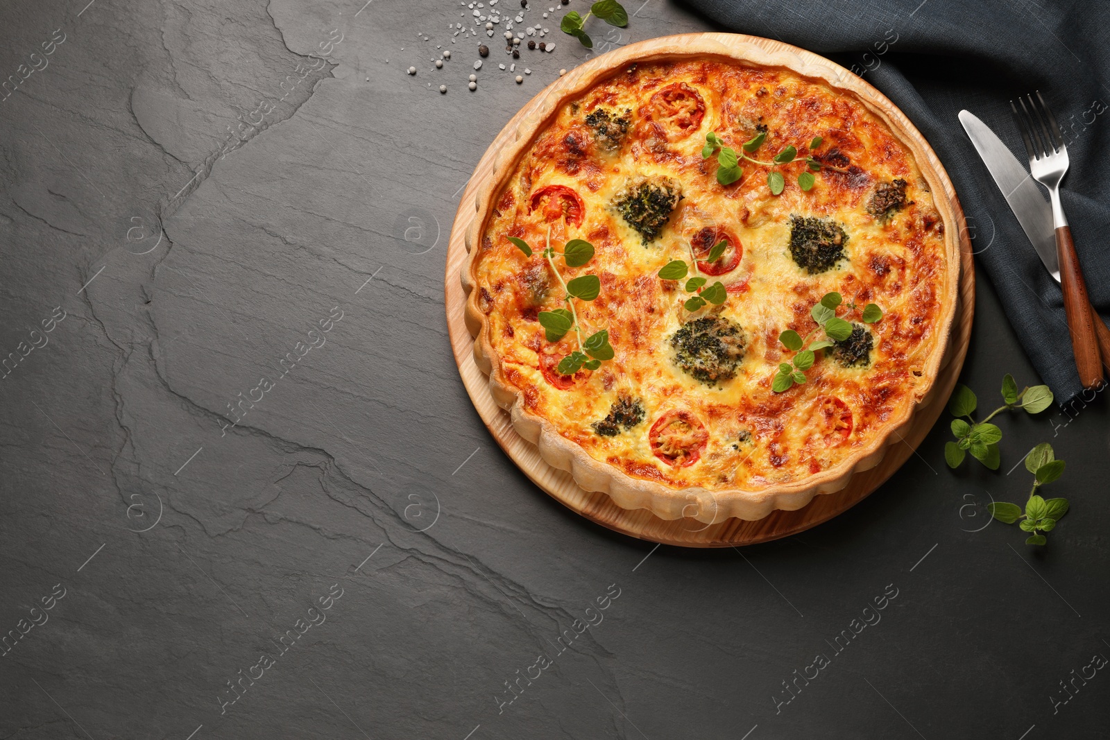 Photo of Delicious homemade vegetable quiche, oregano and cutlery on dark table, flat lay, Space for text