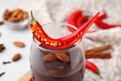 Photo of Glass of hot chocolate with chili pepper and almonds on white table, closeup