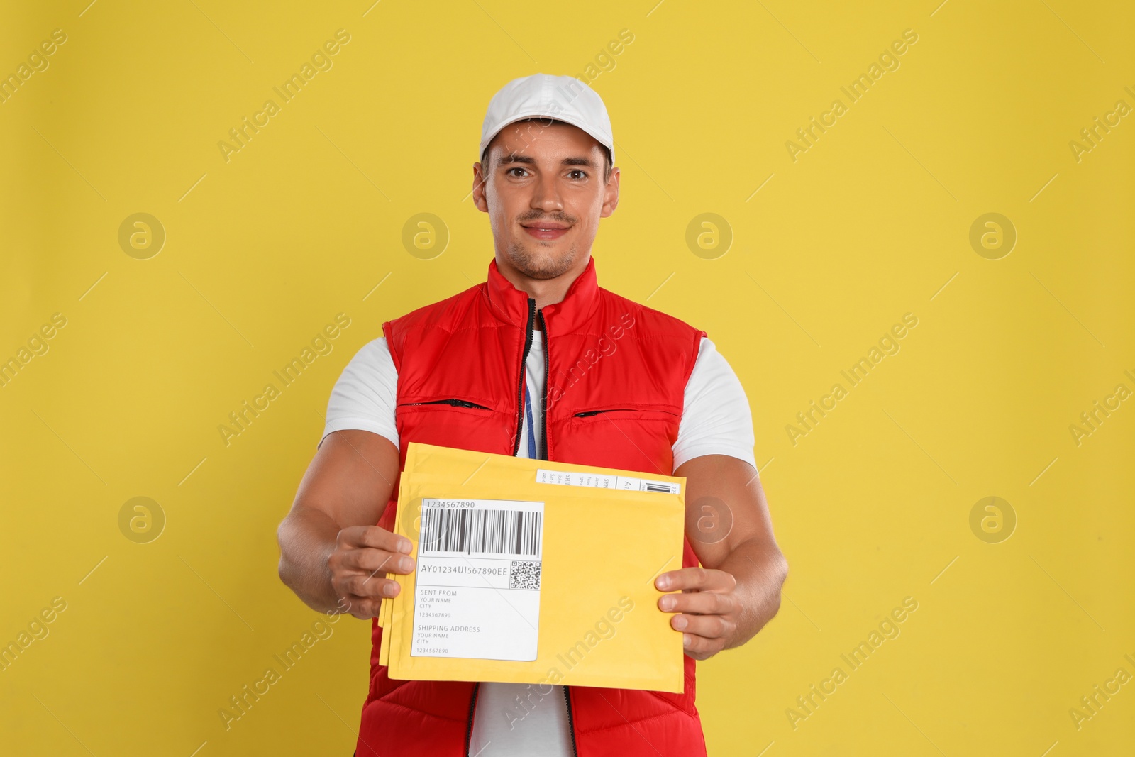 Photo of Happy young courier with envelopes on yellow background