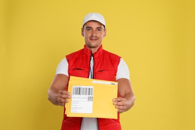 Happy young courier with envelopes on yellow background
