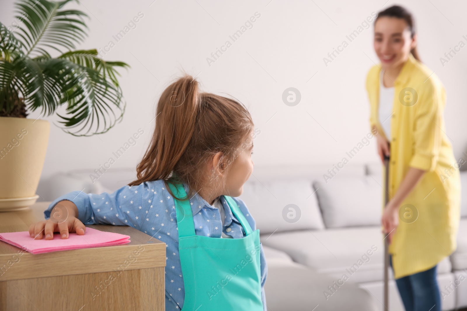 Photo of Little girl helping her mother with cleaning living room