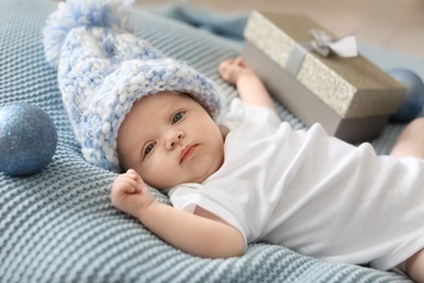 Photo of Cute baby in knitted hat with Christmas decor and gift box lying on blanket
