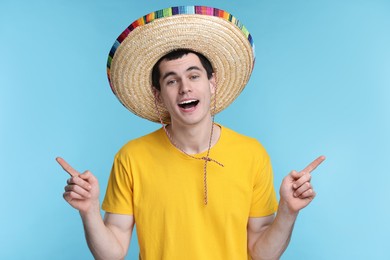 Photo of Young man in Mexican sombrero hat pointing at something on light blue background