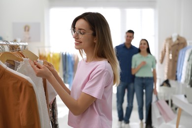 Young woman choosing clothes near rack in modern boutique