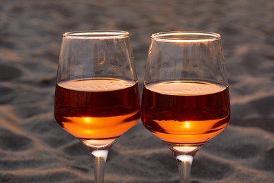 Glasses of tasty rose wine on sand, closeup