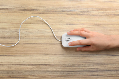 Photo of Woman using modern wired optical mouse on wooden table, top view