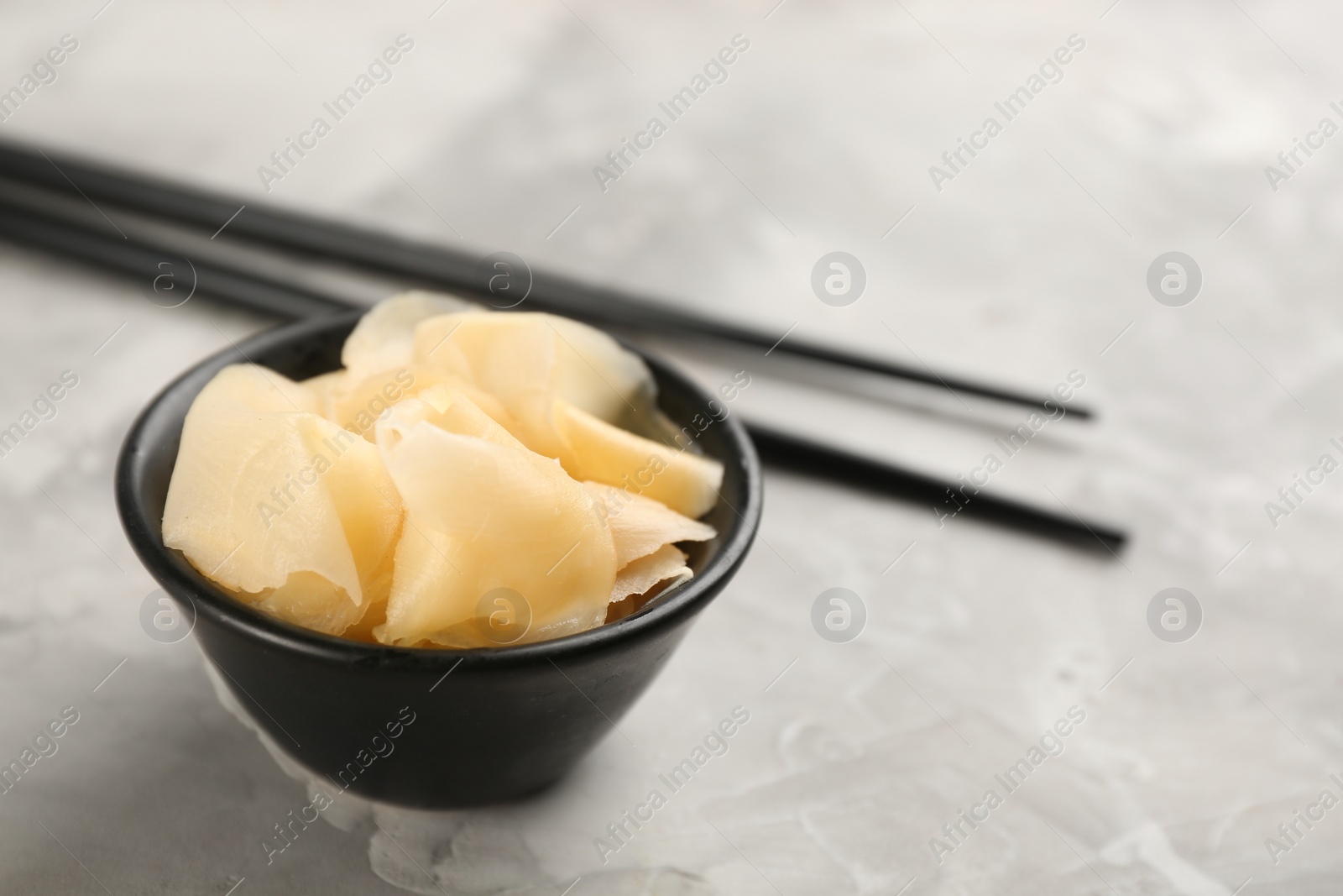 Photo of Spicy pickled ginger and chopsticks on light grey table, space for text