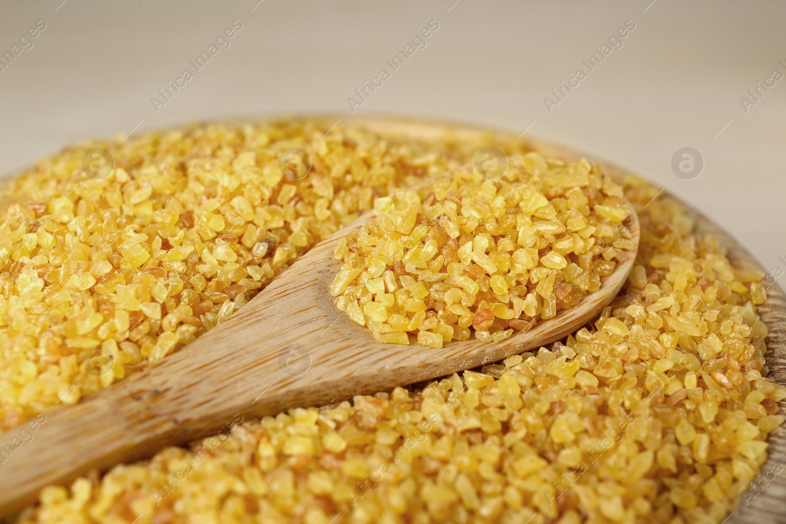 Photo of Bowl and spoon of uncooked bulgur, closeup view