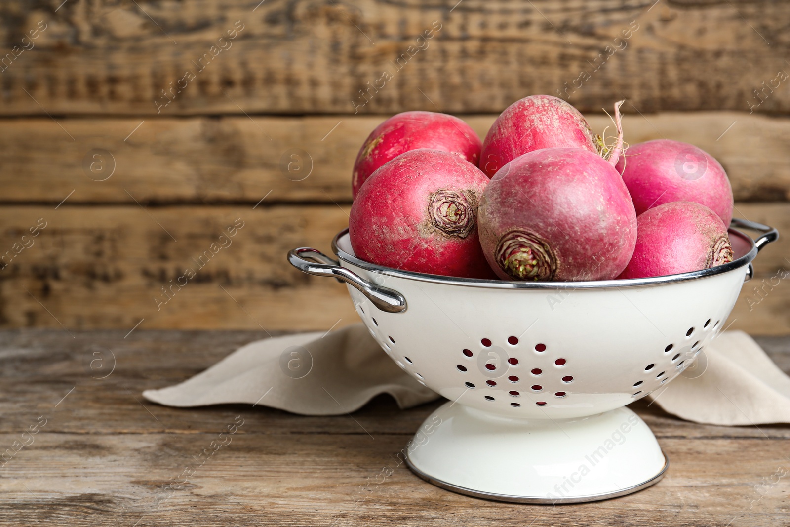 Photo of Colander with red turnips on wooden table. Space for text