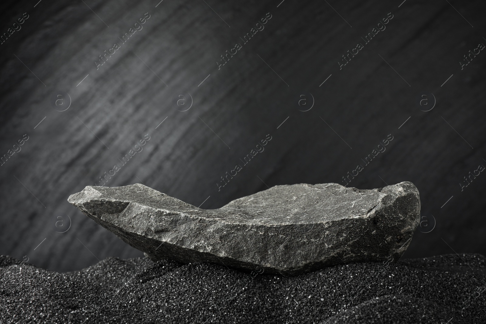 Photo of Presentation of product. Stone podium on black sand against dark textured background. Space for text