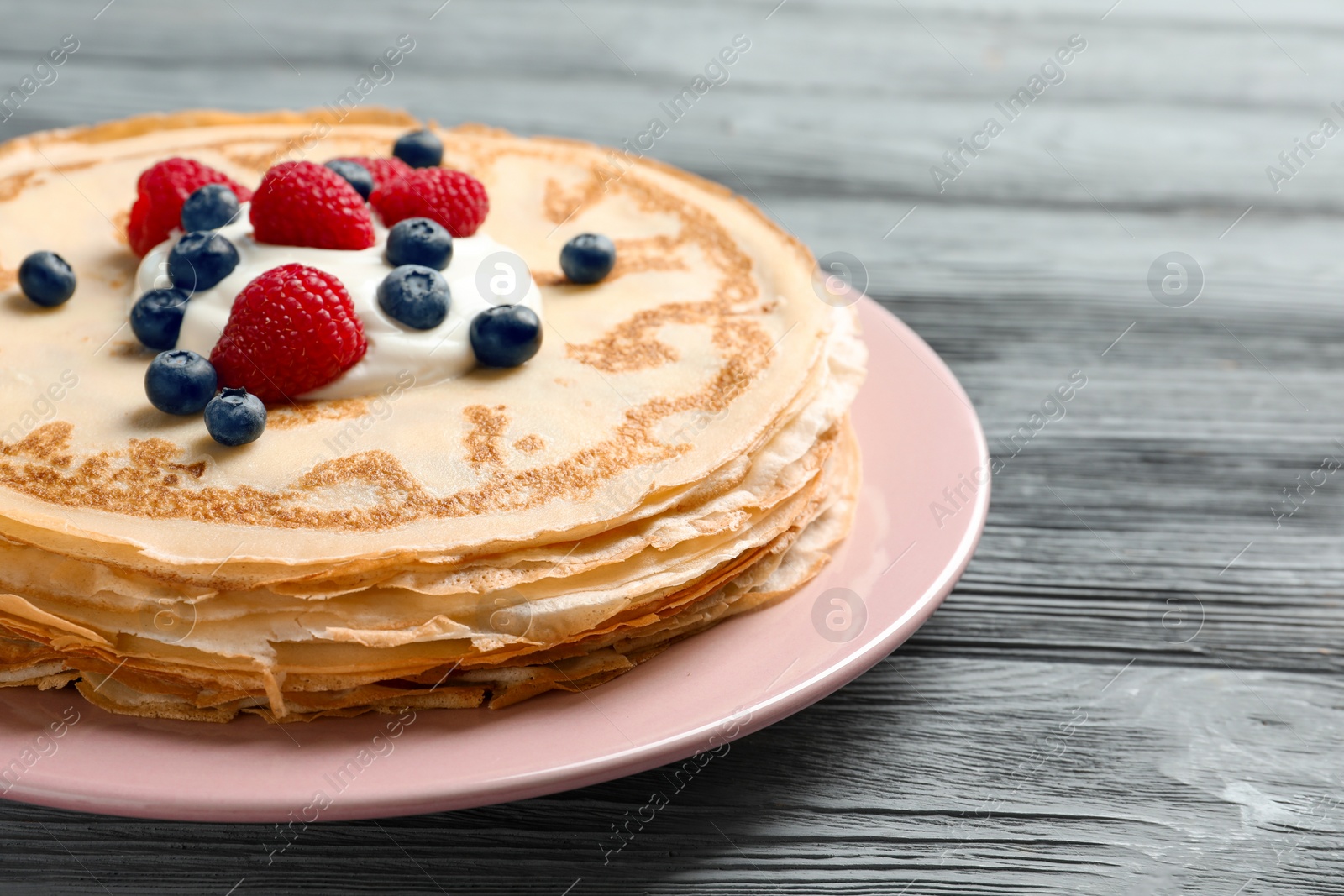 Photo of Thin pancakes served with cream and berries on plate