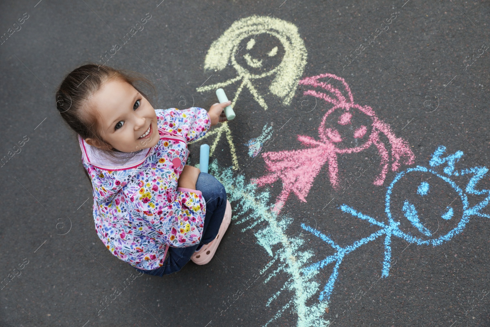 Photo of Child drawing family with chalk on asphalt, above view
