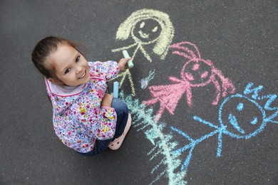 Child drawing family with chalk on asphalt, above view