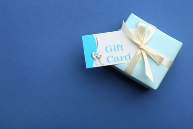 Photo of Gift card and present on blue background, top view. Space for text